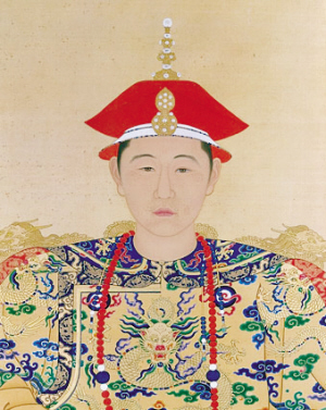 Full-face-view color painting of the head and shoulders of a young man wearing a two-tiered red cap with a white edge, a necklace made of red beads except for two larger blue beads each surrounded by two white beads, and wearing a yellow robe covered with dragon-and-clouds patterns in green, blue, and red.