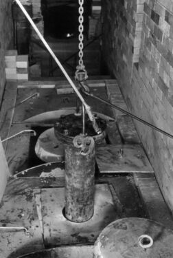 鐵鏈吊着一根柱形容器，容器一部分已沒入下方的設備中。