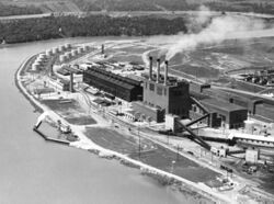 鳥瞰河畔上的工廠廠房，其中一間工廠上有三根冒煙的煙囪。