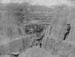 一个挖开的深坑，一名工人靠在坑壁上。